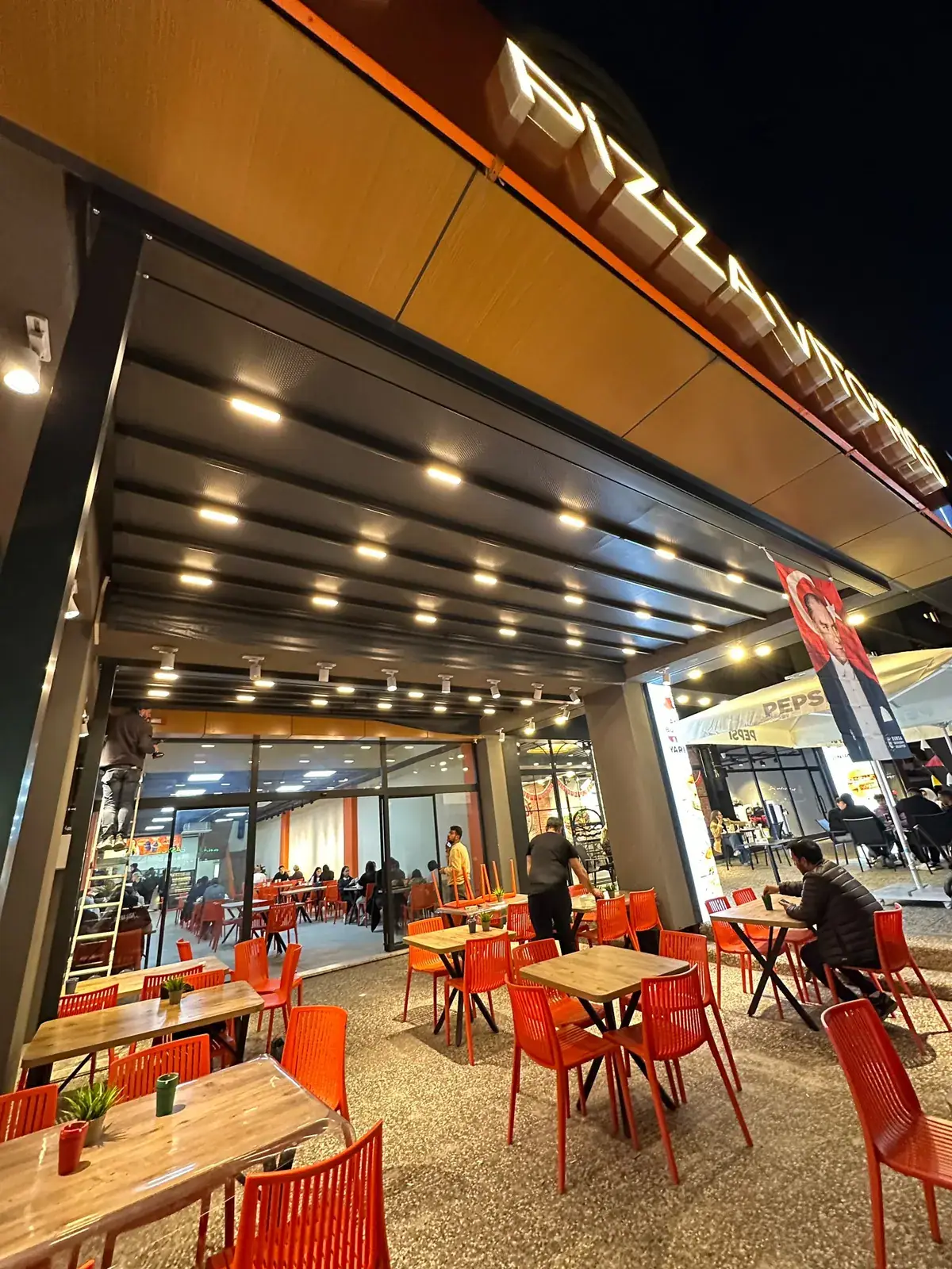 Restoran ön cephesinde LED spotlu antrasit pergola tente, gece görünümü